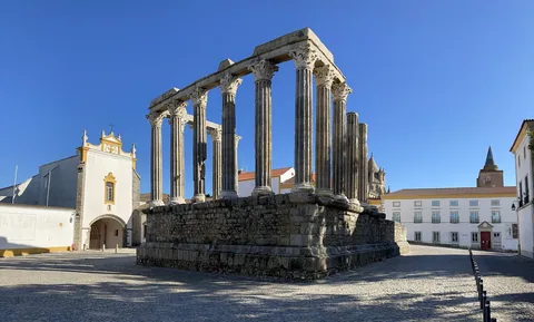 Det romerska templets rad av granitpelare på en hög stensockel, med vita hus och blå himmel bakom