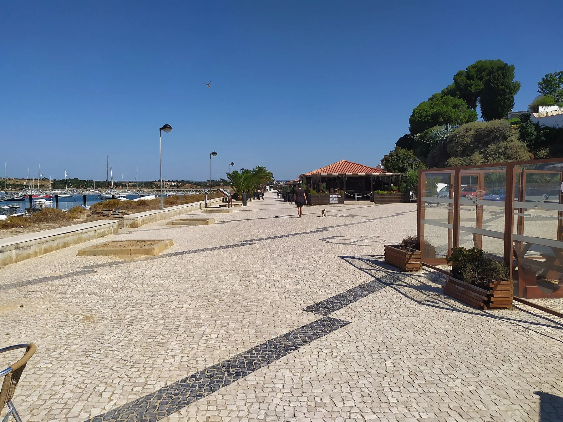 Stenlagd strandpromenad i Alvor med träpaviljonger och bänkar, och lagunen bakom