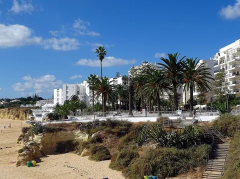 Vita lägenhets- och hotellhus med palmer längs strandpromenaden ovanför en bred sandstrand