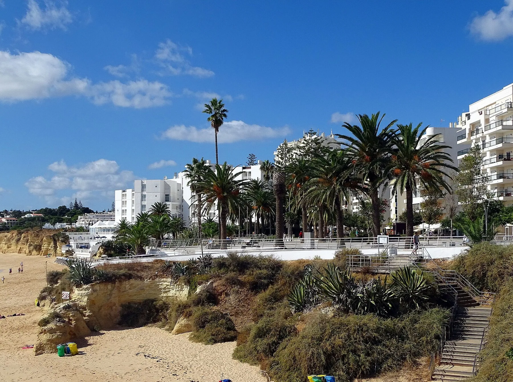Vita lägenhets- och hotellhus med palmer längs strandpromenaden ovanför en bred sandstrand
