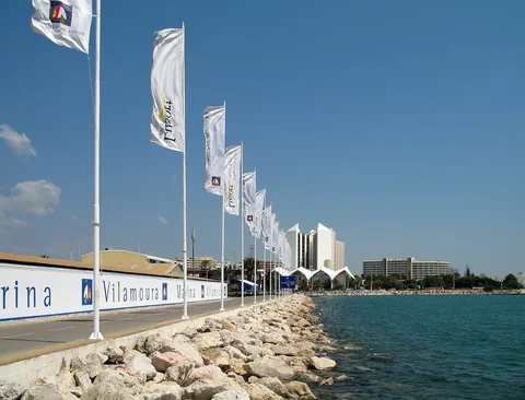 Rad av vita flaggor längs promenaden i Vilamoura, med skylten Marina Vilamoura, stenblock ner mot vattnet och hotellen på andra sidan