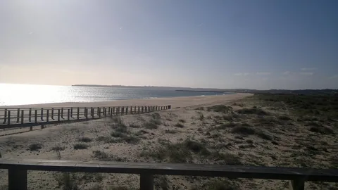 Lång tom sandstrand med träräcke och dyngräs i lågt ljus vid Alvor