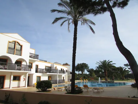 En hotellanläggning i vitt med balkonger runt en pool med fontän, inramad av höga palmer