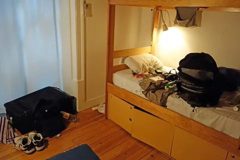 En våningssäng i furu med bäddad underslaf, en ryggsäck på överslafen och resväskor på trägolvet