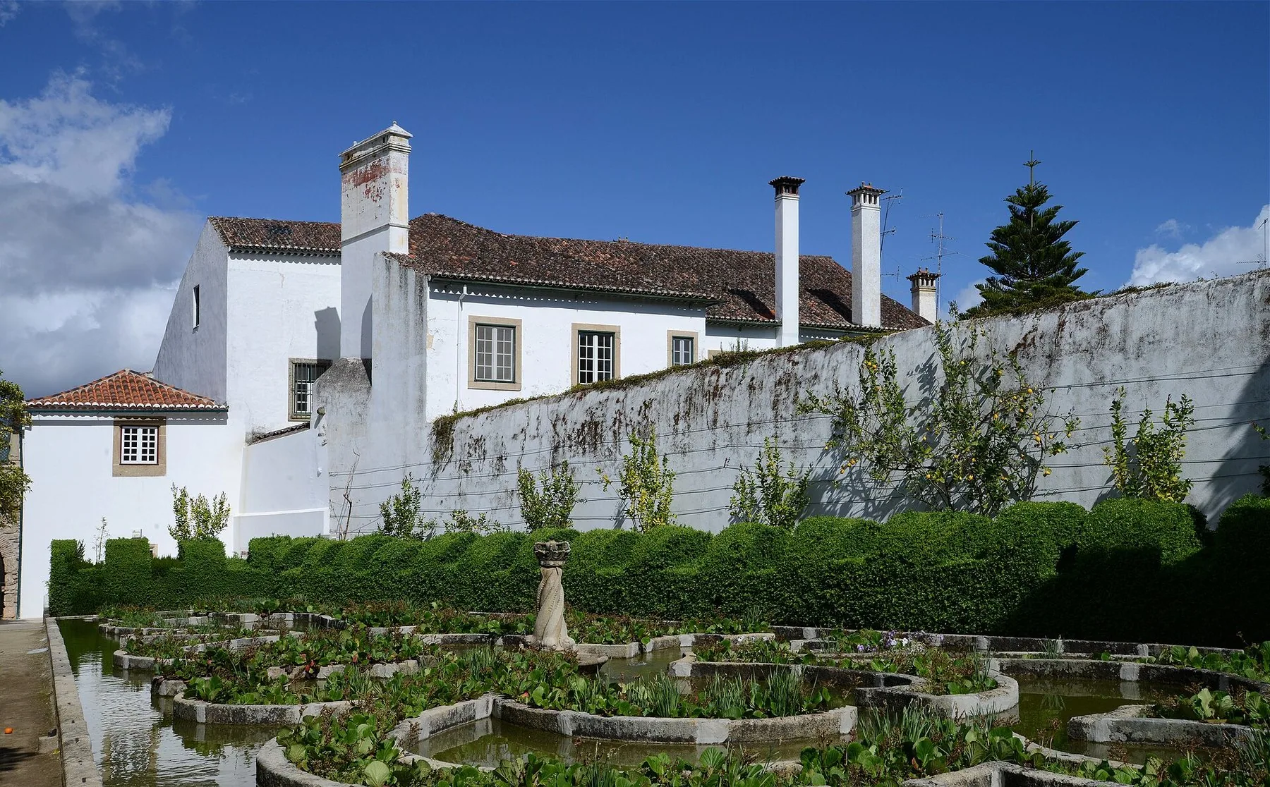 Klippta buxbomshäckar och stenkantade vattenspeglar i biskopspalatsets barockträdgård i Castelo Branco, med palatsets vita länga bakom