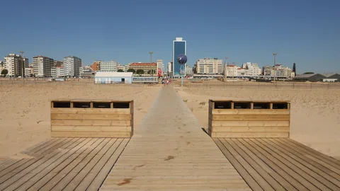 Träspång som löper rakt över en mycket bred sandstrand mot stadens rad av höga vita hus