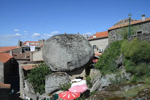 Ett väldigt runt granitblock inklämt mellan tegeltäckta stenhus i en by på en bergssluttning under blå himmel