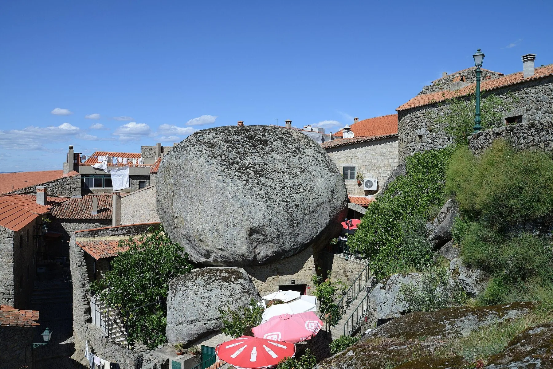Ett väldigt runt granitblock inklämt mellan tegeltäckta stenhus i en by på en bergssluttning under blå himmel