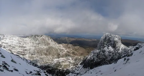Snöklädda bergssidor och en brant klippformation i Serra da Estrela under tunga moln