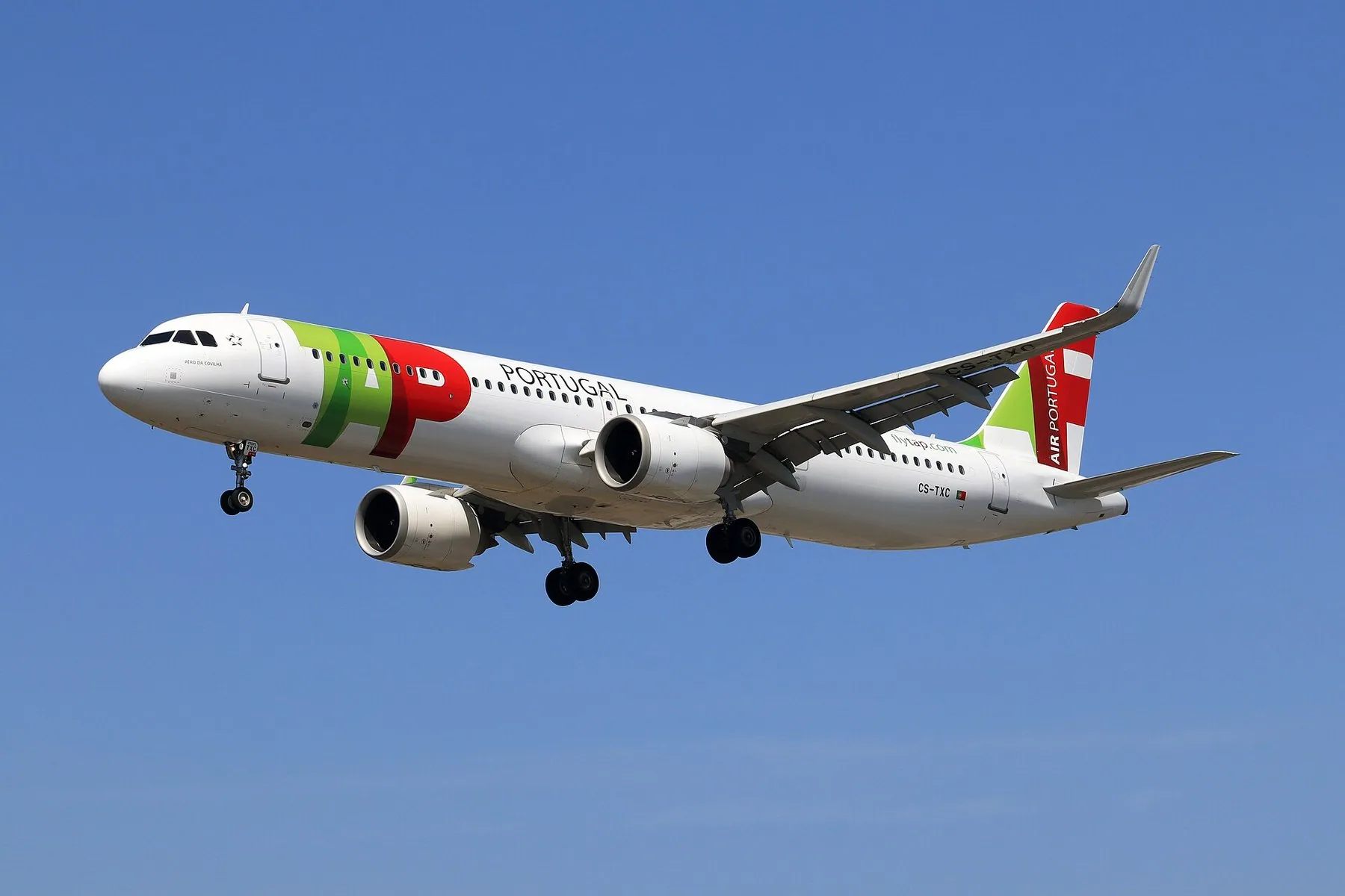 Ett vitt trafikflygplan med TAP Air Portugals gröna och röda dekor stiger mot blå himmel med landningsstället utfällt