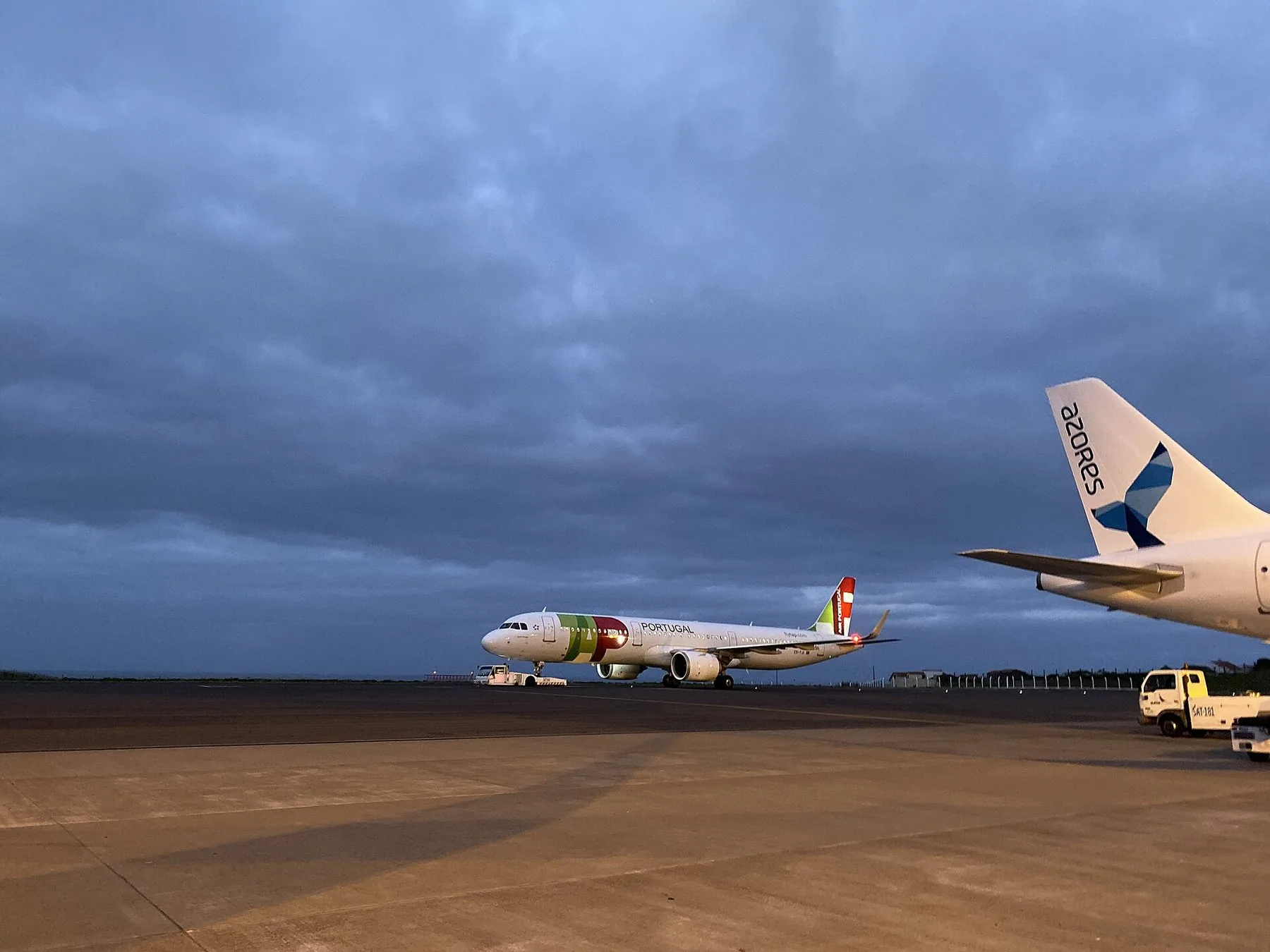Ett flygplan från TAP Air Portugal står på plattan i Ponta Delgada under mörka skymningsmoln, med stjärten på ett Azores-plan i förgrunden