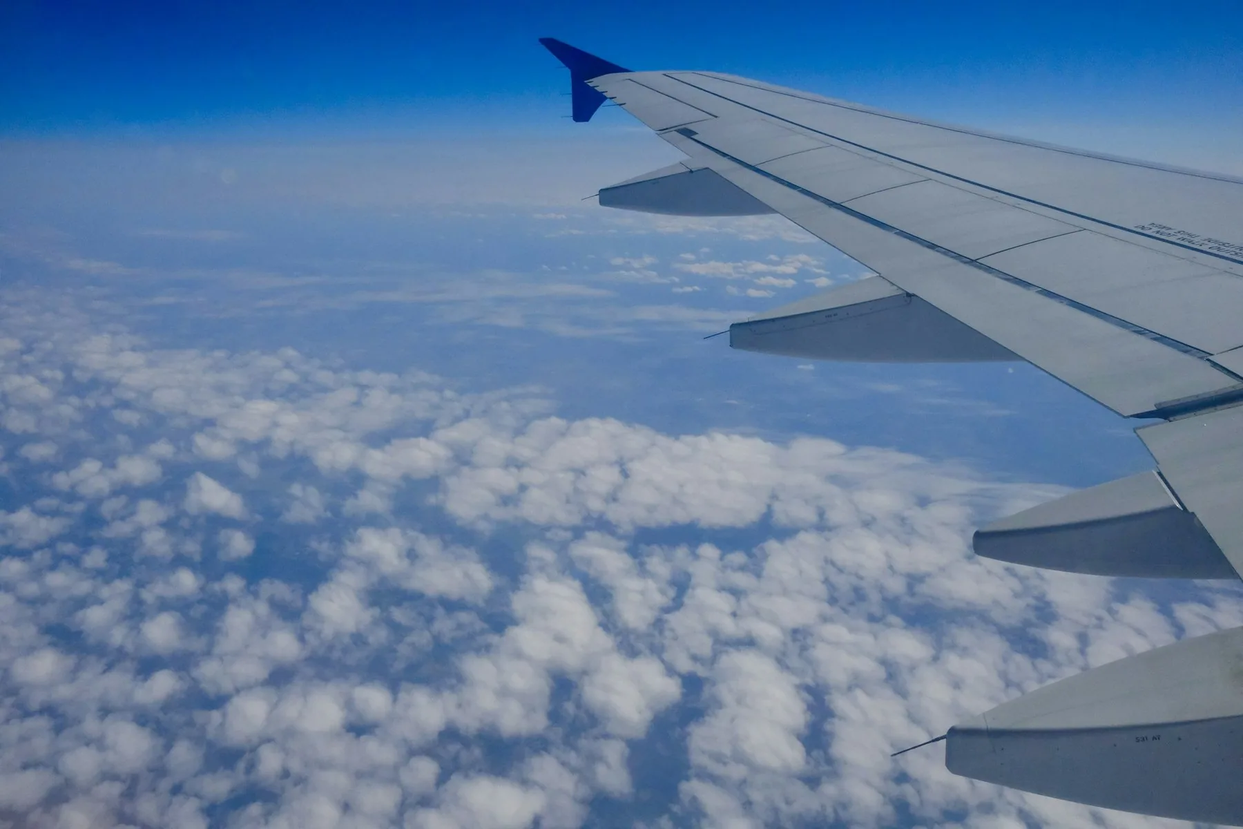 Flygplansvinge över ett molntäcke med djupblå himmel ovanför