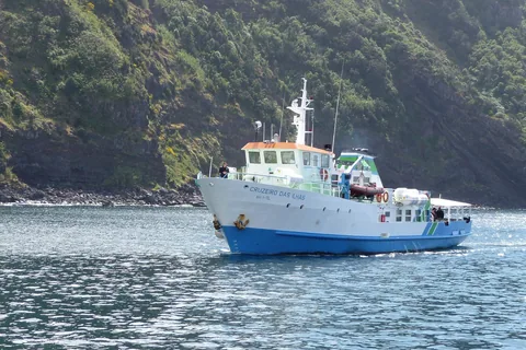 Blå och vit passagerarfärja på väg längs en brant grön kust på Azorerna