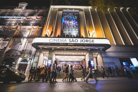 Den upplysta entrén till en biograf med skylten Cinema São Jorge över markisen, en filmfestivalaffisch på fasaden och besökare på trappan