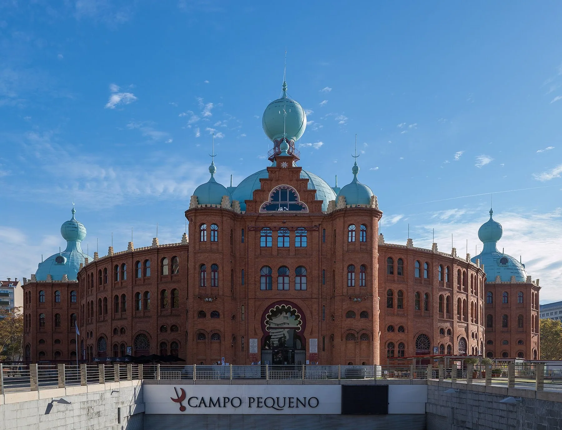 Arenan Campo Pequeno i Lissabon sedd utifrån: en cirkelrund tegelbyggnad i morisk stil med hästskobågar och turkosa lökkupoler mot blå himmel