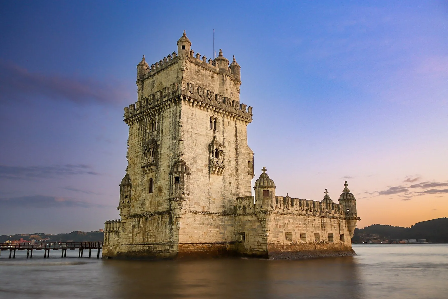 Torre de Belém reser sig ur stilla vatten i gyllene kvällsljus mot en rosafärgad himmel