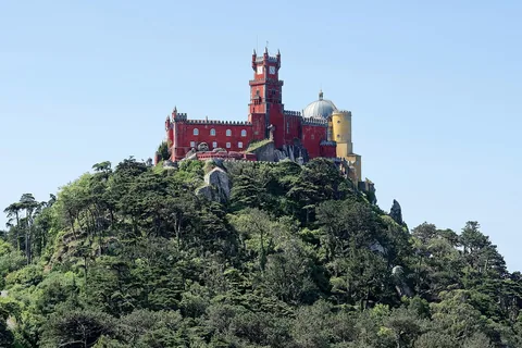 Palácio da Pena i rött och gult kröner en tätt skogklädd bergstopp under klarblå himmel
