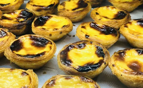 Nybakade pastéis de nata med karamelliserad yta och frasig smördeg tätt intill varandra