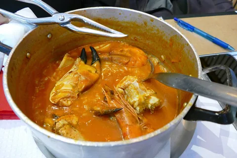Arroz de marisco i en gryta på bordet: blött orange ris med krabbklor, räkor och musslor i rikligt med spad