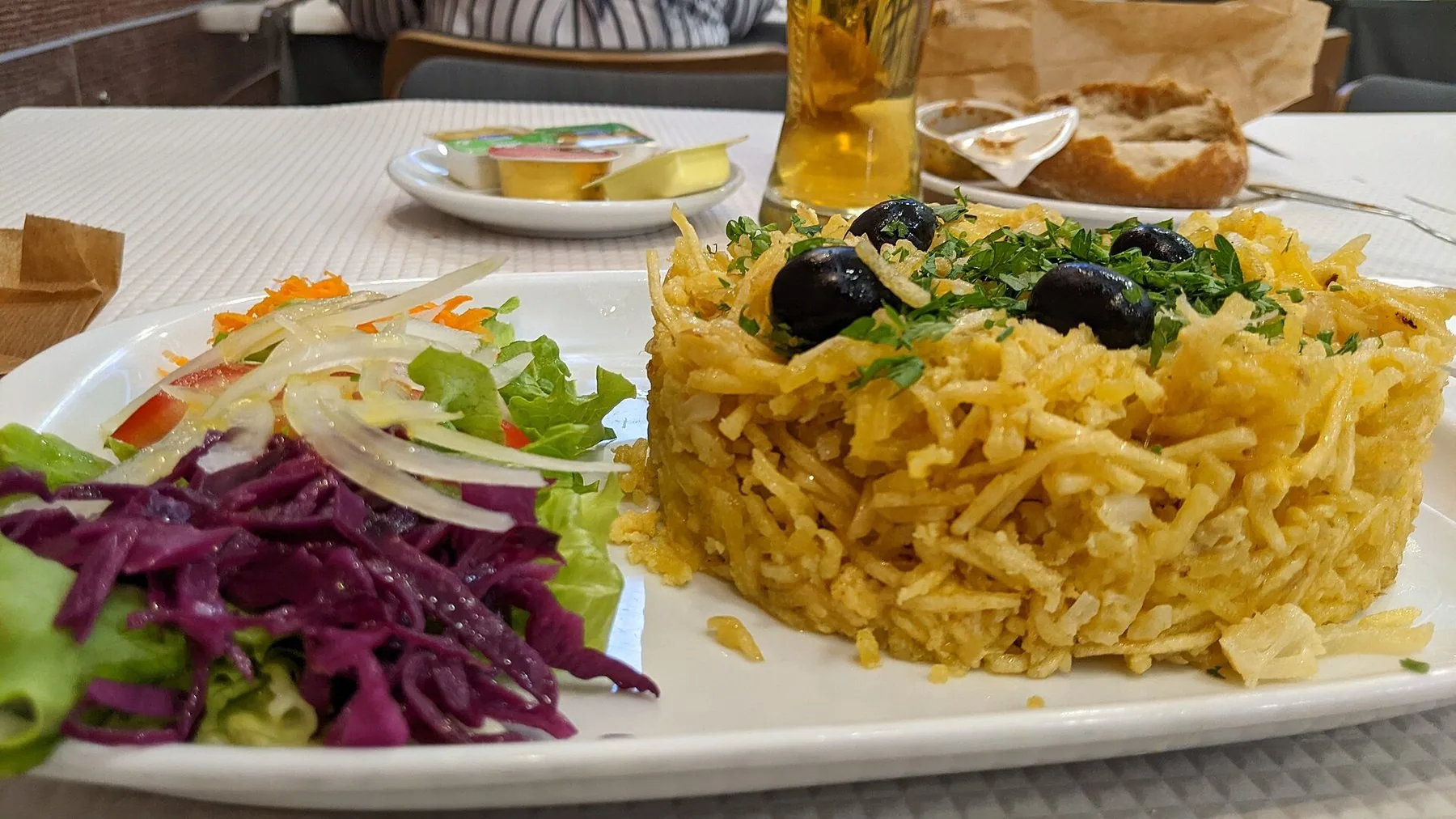 Bacalhau à Brás av strimlad torsk, potatis och ägg med svarta oliver, serverad på tallrik med sallad vid sidan