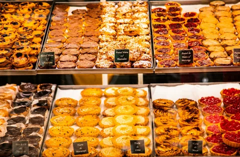 Kyldisk i ett portugisiskt bageri med brickor av bakverk i rader, märkta pastel de nata, tarte de lima och tarte de maçã på små svarta skyltar