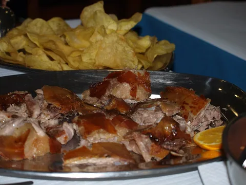 Uppskuret spädgrisstek med spröd svål på ett fat, med chips och en apelsinskiva bredvid