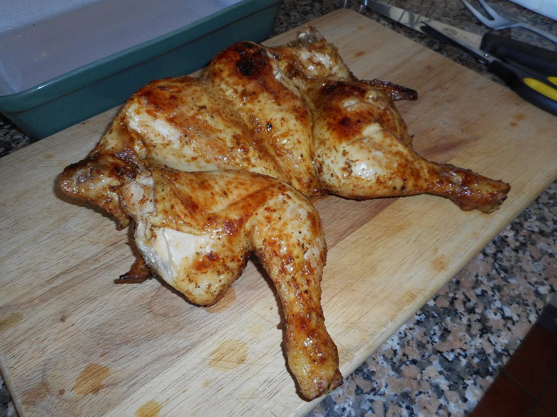 En hel grillad kyckling som fläkts ut och penslats med rödorange kryddblandning, upplagd på en träskiva