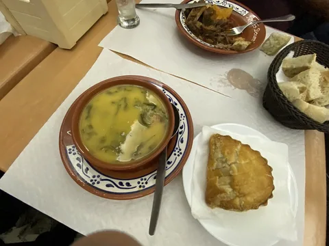 En lerskål med grön soppa på ett bord, med bröd i korg och en gyllene friterad pastej bredvid