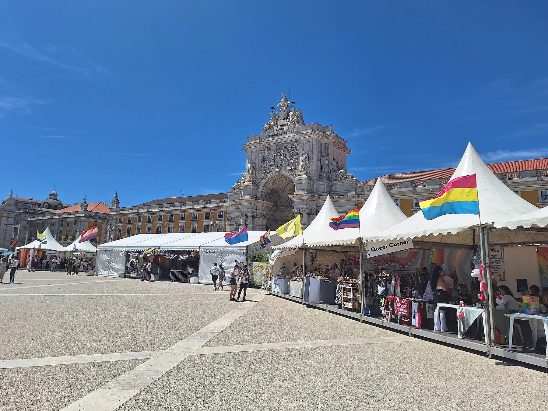 Regnbågsflaggor vajar på vita marknadstält framför triumfbågen vid Rua Augusta i Lissabon en solig dag