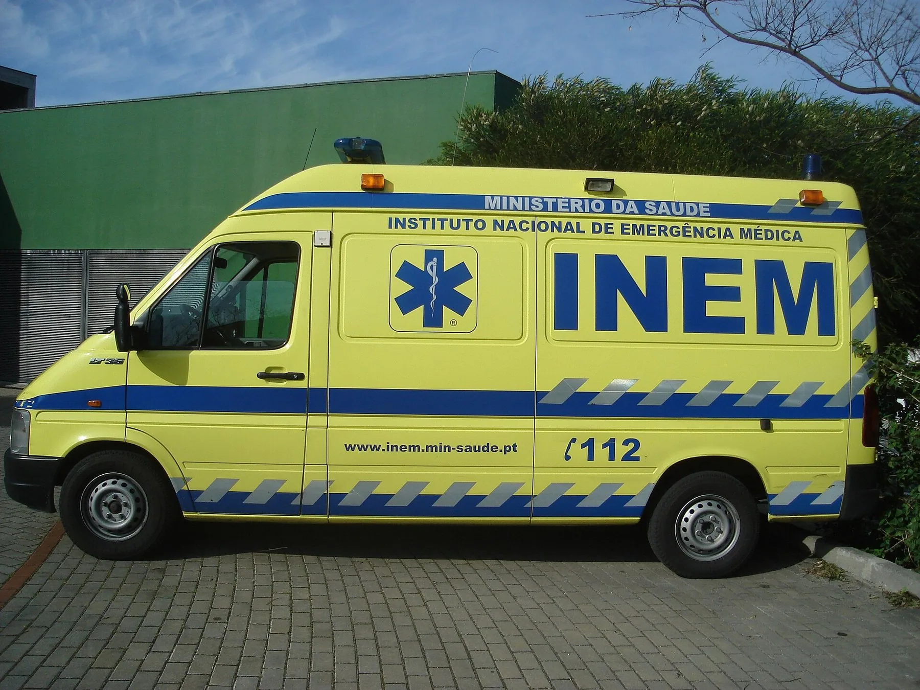 Gul ambulans från INEM sedd från sidan, märkt med nödnumret 112 och Instituto Nacional de Emergência Médica