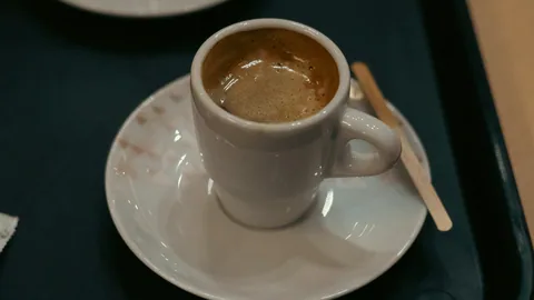 En liten kopp espresso på vitt fat på ett grönt kafébord