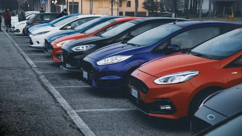 En lång rad småbilar i olika färger parkerade tätt intill varandra i sned vinkel på en asfalterad parkering