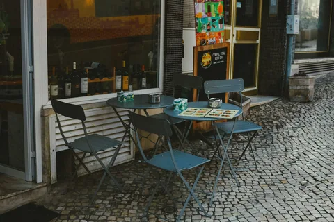 Blå bord och stolar på en kullerstenstrottoar utanför en restaurang