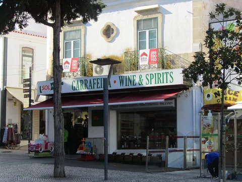 En butik med skylten Garrafeira Wine & Spirits över entrén och rader av vin- och spritflaskor i skyltfönstret