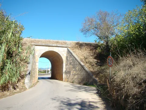 Smal asfaltväg som passerar under en stenvalvsbro i Algarves inland