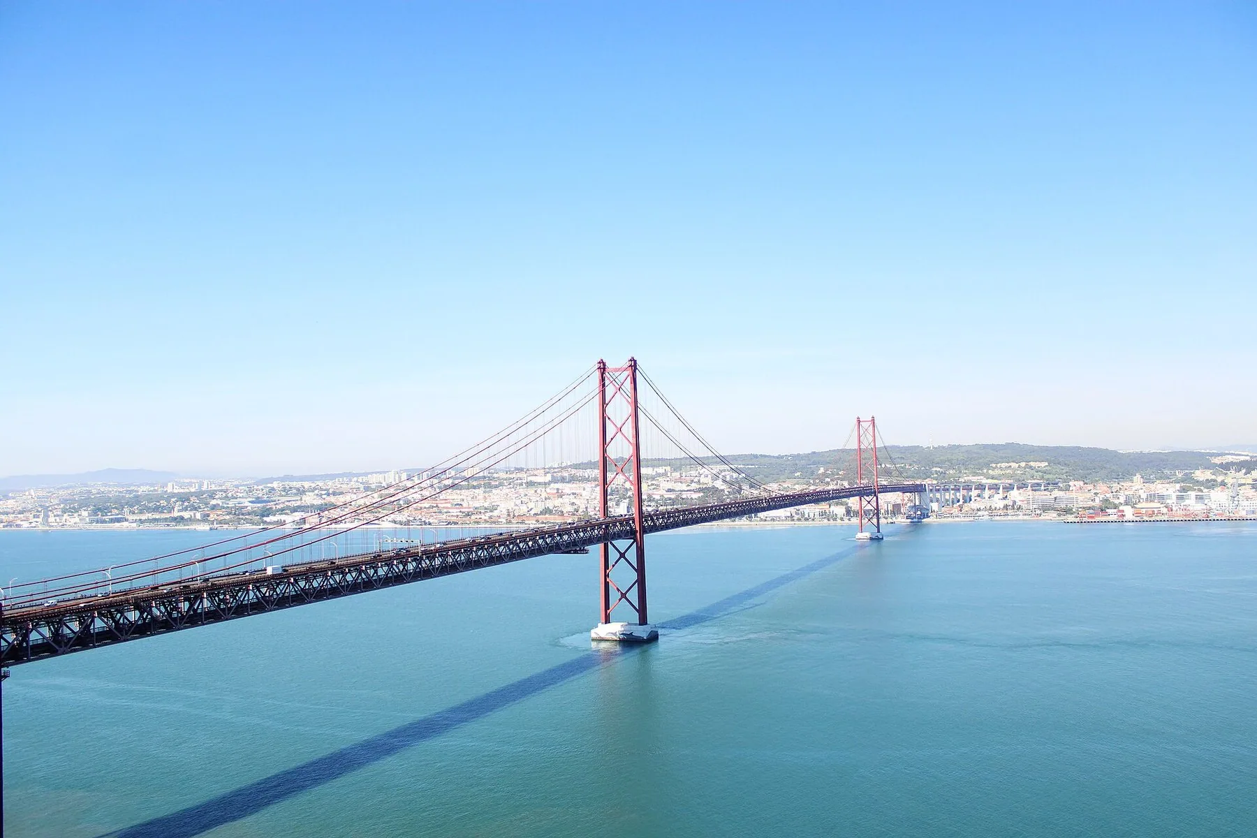 Ponte 25 de Abril spänner över Tejo i klart solsken, med Lissabons bebyggelse längs andra stranden