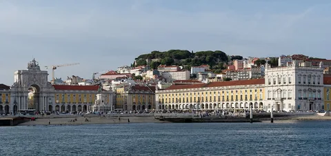 Praça do Comércio sett från Tejo, med gula arkadbyggnader längs vattnet och slottskullen bakom