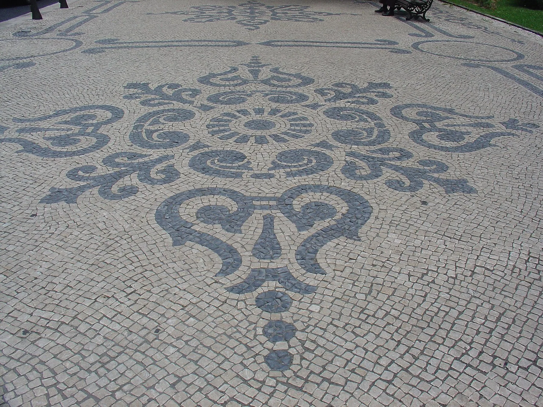 Portugisisk mosaikgatsten där mörka stenar bildar ett stort snirkligt ornament i den ljusa kalkstenen