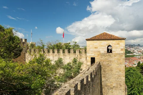 Castelo de São Jorges tinnkrönta mur och fyrkantiga torn med portugisisk flagga, med Lissabons tegeltak nedanför till höger