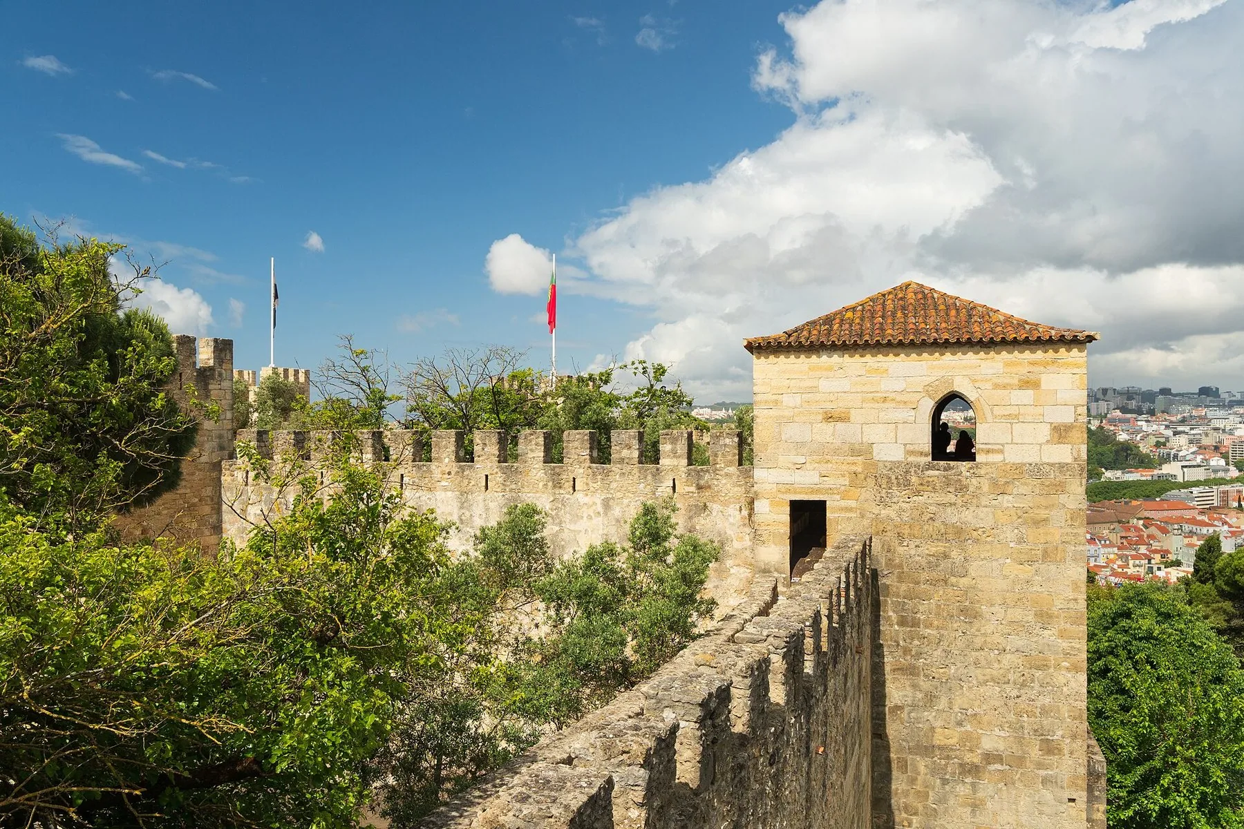 Castelo de São Jorges tinnkrönta mur och fyrkantiga torn med portugisisk flagga, med Lissabons tegeltak nedanför till höger