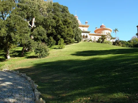 Palácio de Monserrate med kupol och hästskobågar högst upp på en grön gräsluttning, med en kullerstensgång genom parken i förgrunden