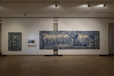 En lång blåvit kakelpanel med jaktmotiv monterad på en vit vägg i en tom museisal