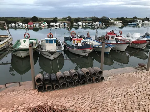 Små färgade fiskebåtar förtöjda i rad längs kajen i Fuseta, speglade i stilla vatten
