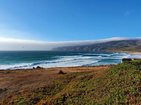 Praia do Guincho vid Cascais: rad efter rad av brytande vågor rullar in mot den vidsträckta sandstranden, med Sintrabergens siluett bakom.