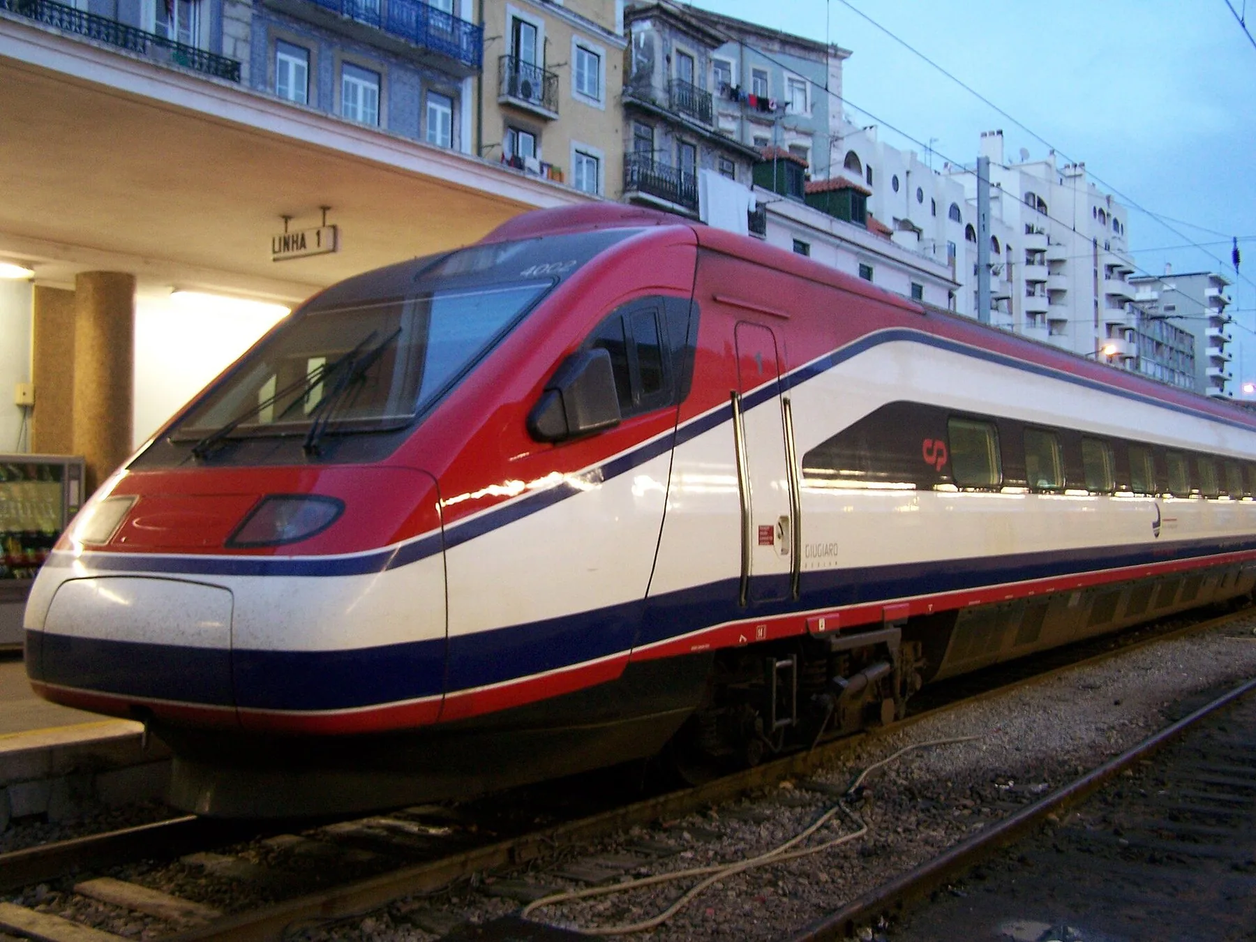 Ett rött, vitt och blått Alfa Pendular-tåg med CP:s logotyp står vid spår 1 på en station i Lissabon i skymningen
