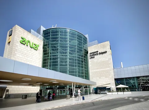 Terminalentrén på Lissabons flygplats med rund glasfasad och skylten Aeroporto Humberto Delgado, med av- och påstigningsfilen under skärmtaket