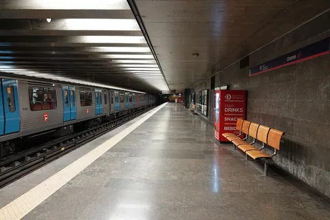 En tunnelbaneperrong med ett blått tåg vid spåret, orange sittplatser och skylten Oriente på väggen