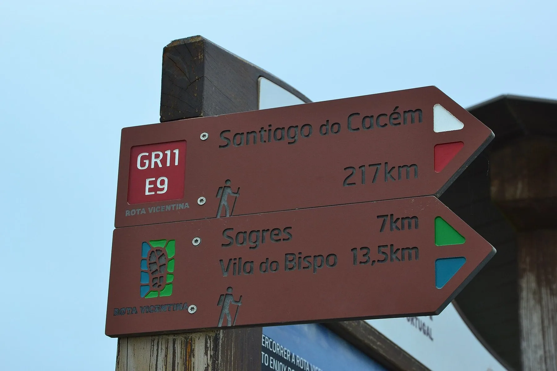Vägvisare i brunt trä för Rota Vicentina och fjärrleden GR11/E9: Santiago do Cacém 217 km åt ett håll, Sagres 7 km och Vila do Bispo 13,5 km åt det andra.